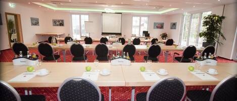 A conference room with multiple tables, chairs, and a projector screen.