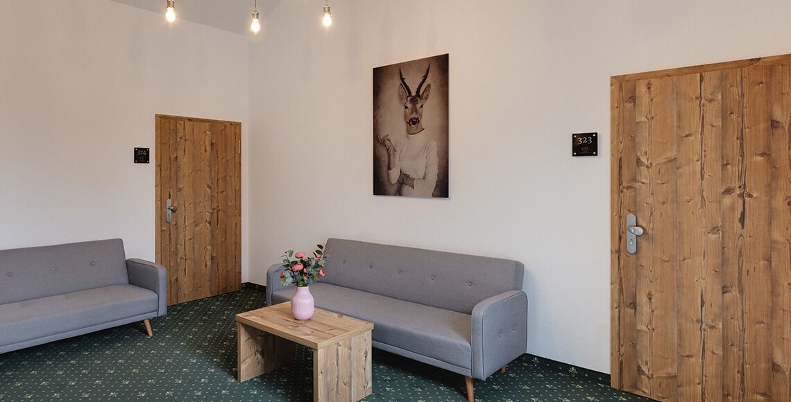 Una habitació amb dos sofàs grisos, una taula de centre de fusta amb un vas rosa i una porta de fusta amb una placa identificadora.