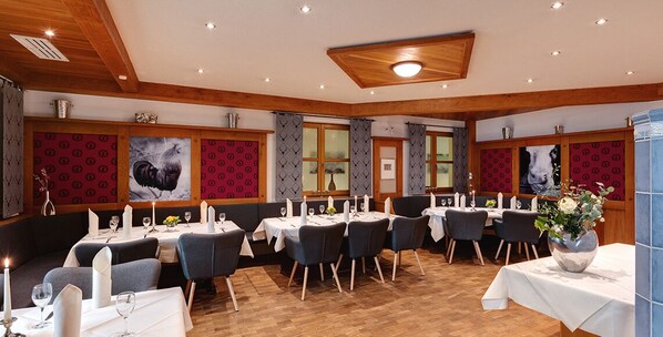 A restaurant with wooden beams, red patterned wallpaper, and multiple tables set for dining.