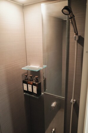 Et moderne badeværelse med en glashylde med toiletartikler, en bruser med håndbruserspjæt og en metallisk hane.