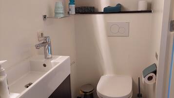 Un baño pequeño con un lavamanos blanco, un inodoro y un cesto de basura.