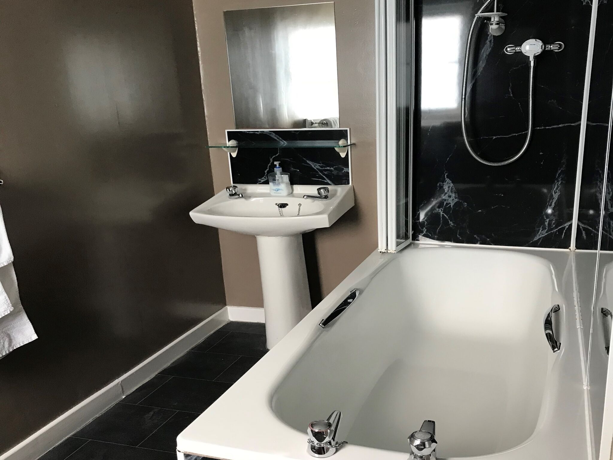 Un baño moderno con una bañera blanca, un lavamanos pedestal y una zona de ducha con mampara de vidrio.