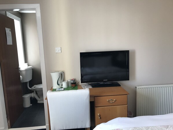 A hotel room with a bed, a desk with a television, a coffee maker, and a radiator.