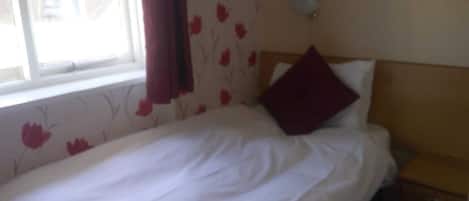 A single bed with white bedding, a wooden headboard, and a nightstand with a drawer.
