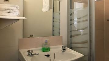 Een badkamer met een wit wastafel, een spiegel en een douchecabine van glas.