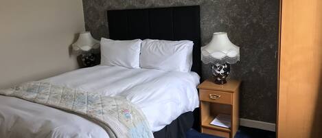 A neatly made bed with white linens, a dark headboard, and a blue patterned carpet.
