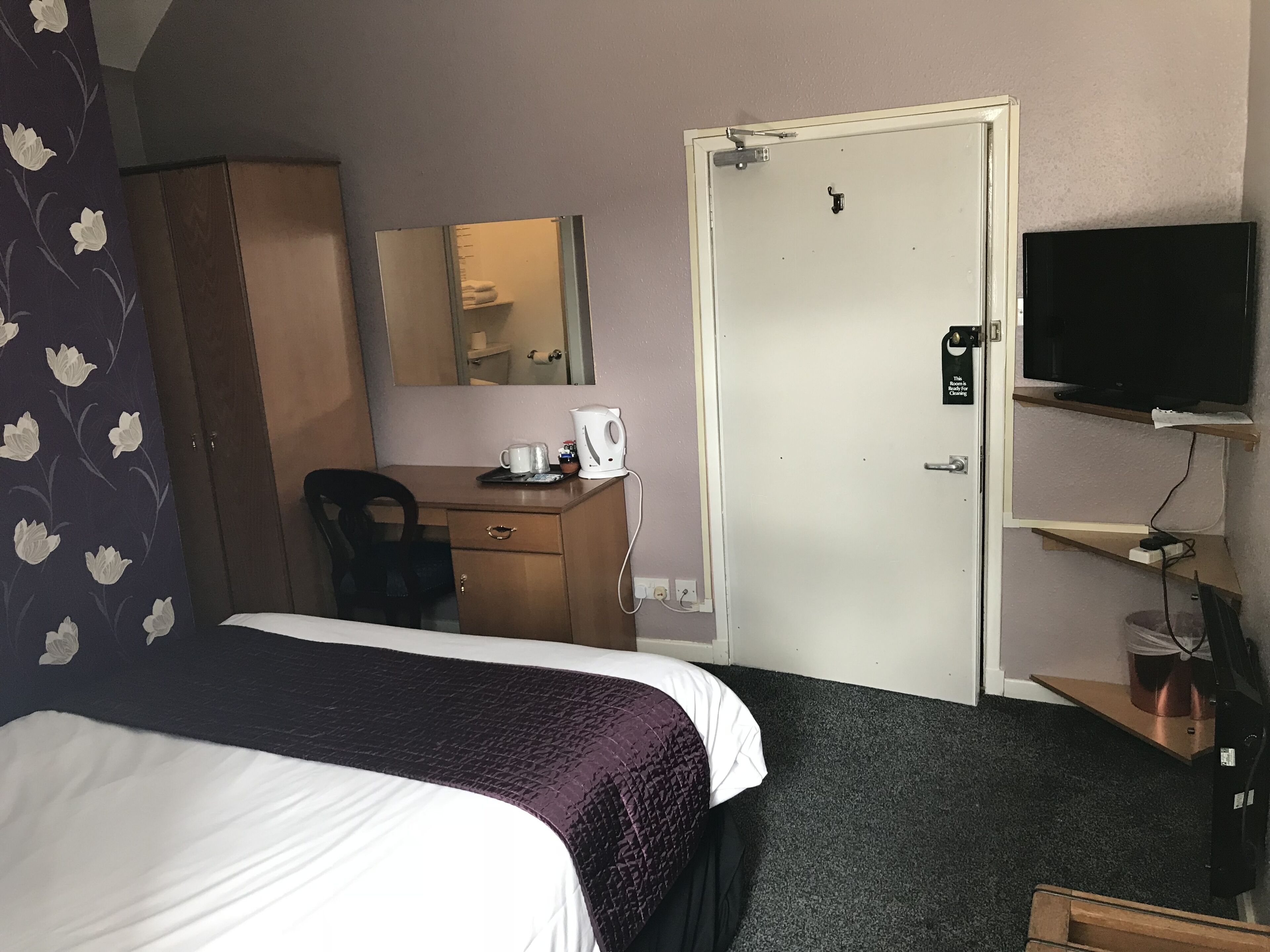 A hotel room with a bed, a desk, a chair, a wardrobe, a television, and a mirror.
