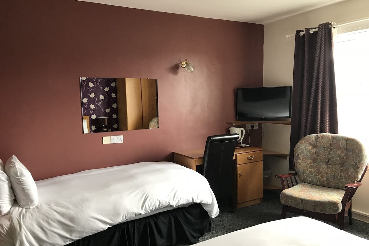 A hotel room with two beds, a desk with a chair, a television, and a mirror on the wall.