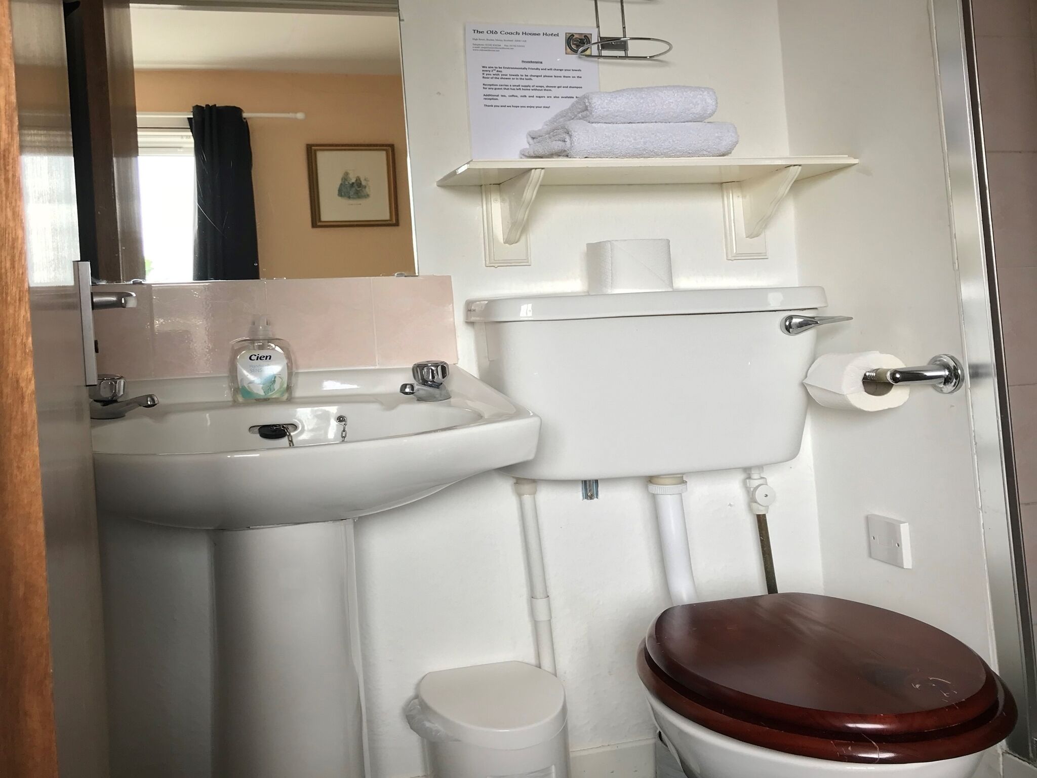 Ein Badezimmer mit Waschbecken, Toilette und Ablage über der Toilette, auf der ein Handtuch liegt.