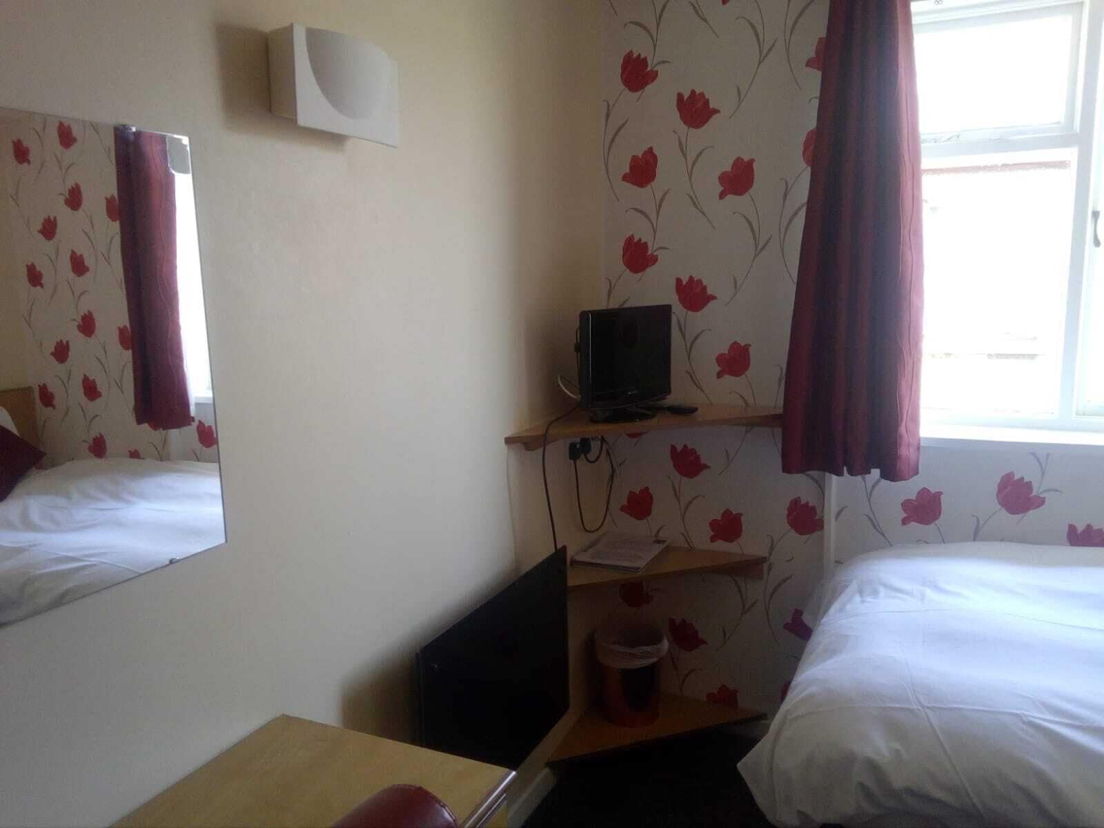 A hotel room with two beds, a TV on a shelf, a mirror, and a window with curtains.
