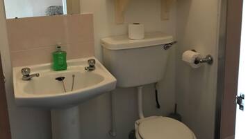 Un baño con lavamanos, inodoro y un estante con toallas.