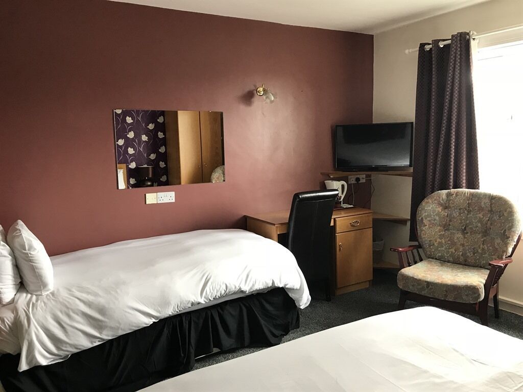 Ein Hotelzimmer mit einem Bett, einem Schreibtisch mit Computer, einem Stuhl, einem Fernseher und einem Fenster mit Vorhängen.