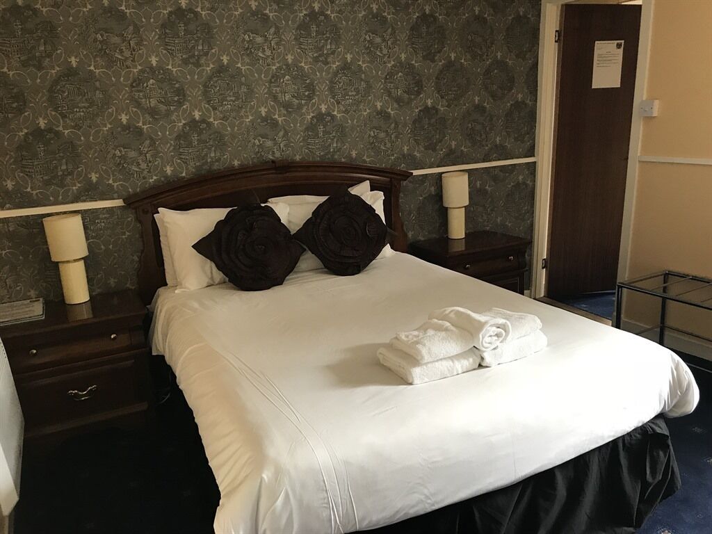 A neatly made bed with white linens, two dark pillows, and folded towels on a wooden headboard.