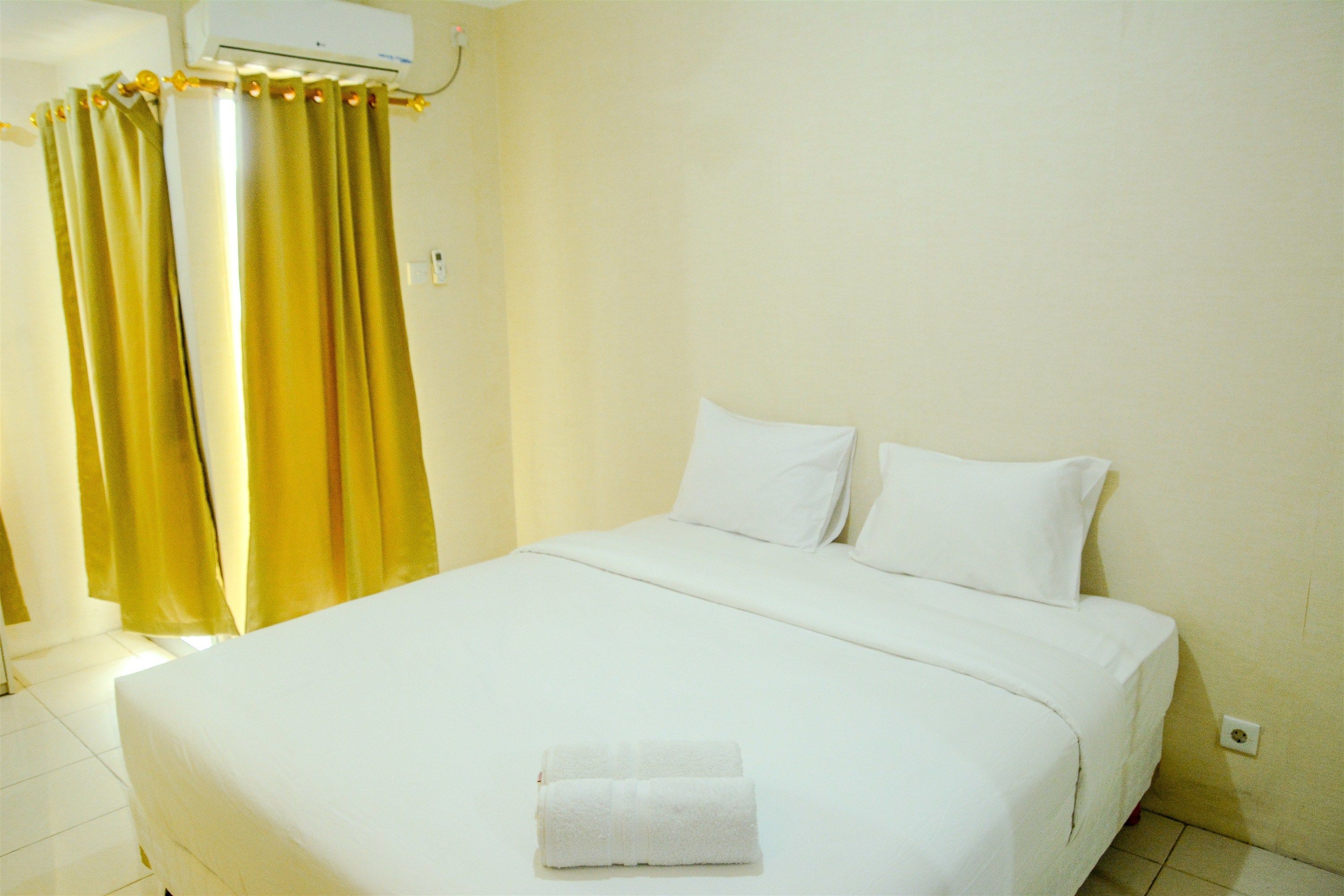 A hotel room with a bed, white bedding, a white towel, and yellow curtains.