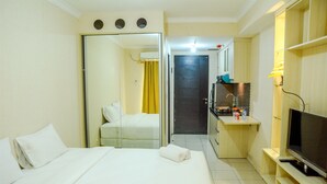 Ein Hotelzimmer mit Bett, Fernseher, einer kleinen Küchenzeile und einem Badezimmer mit Spiegel und gelbem Vorhang.
