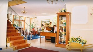 A spacious living area with a staircase, a piano, a wooden cabinet, and a flower cart.