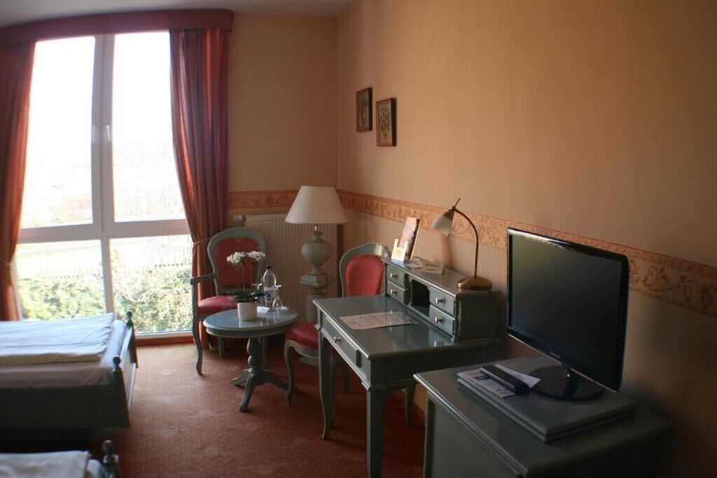 Una habitación de hotel con una cama, un escritorio con computadora, una silla, una lámpara y una ventana con cortinas.