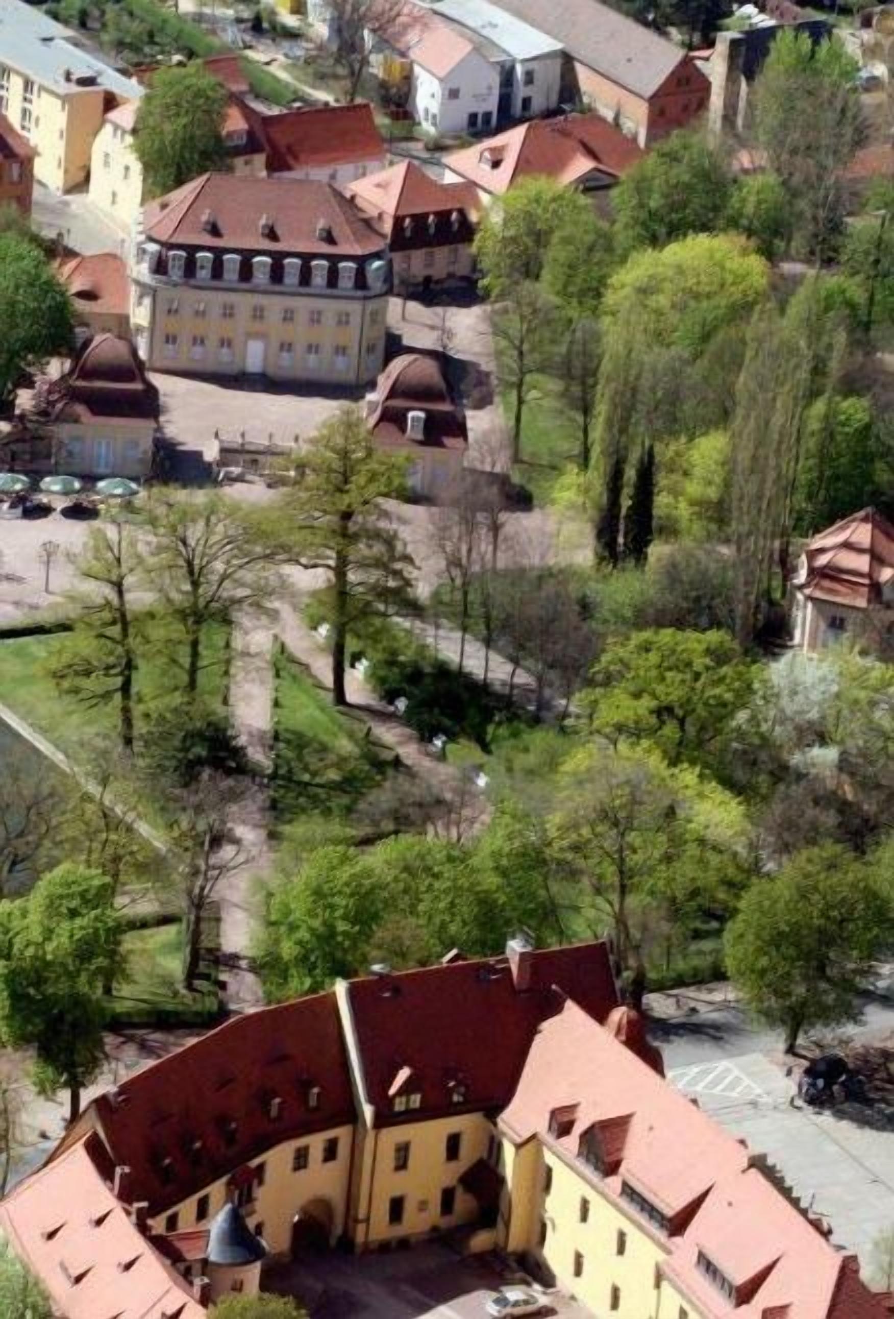 Ein historisches Gebäude mit einem zentralen Innenhof, umgeben von Bäumen und weiteren Gebäuden.