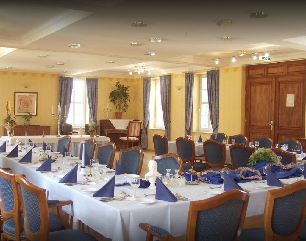 Ein eleganter Speisesaal mit mehreren gedeckten Tischen, blaues Servietten, weiße Tischdecken und Holzsessel.