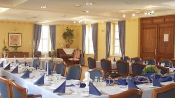 Ein eleganter Speisesaal mit mehreren gedeckten Tischen, blaues Servietten, weiße Tischdecken und Holzsessel.