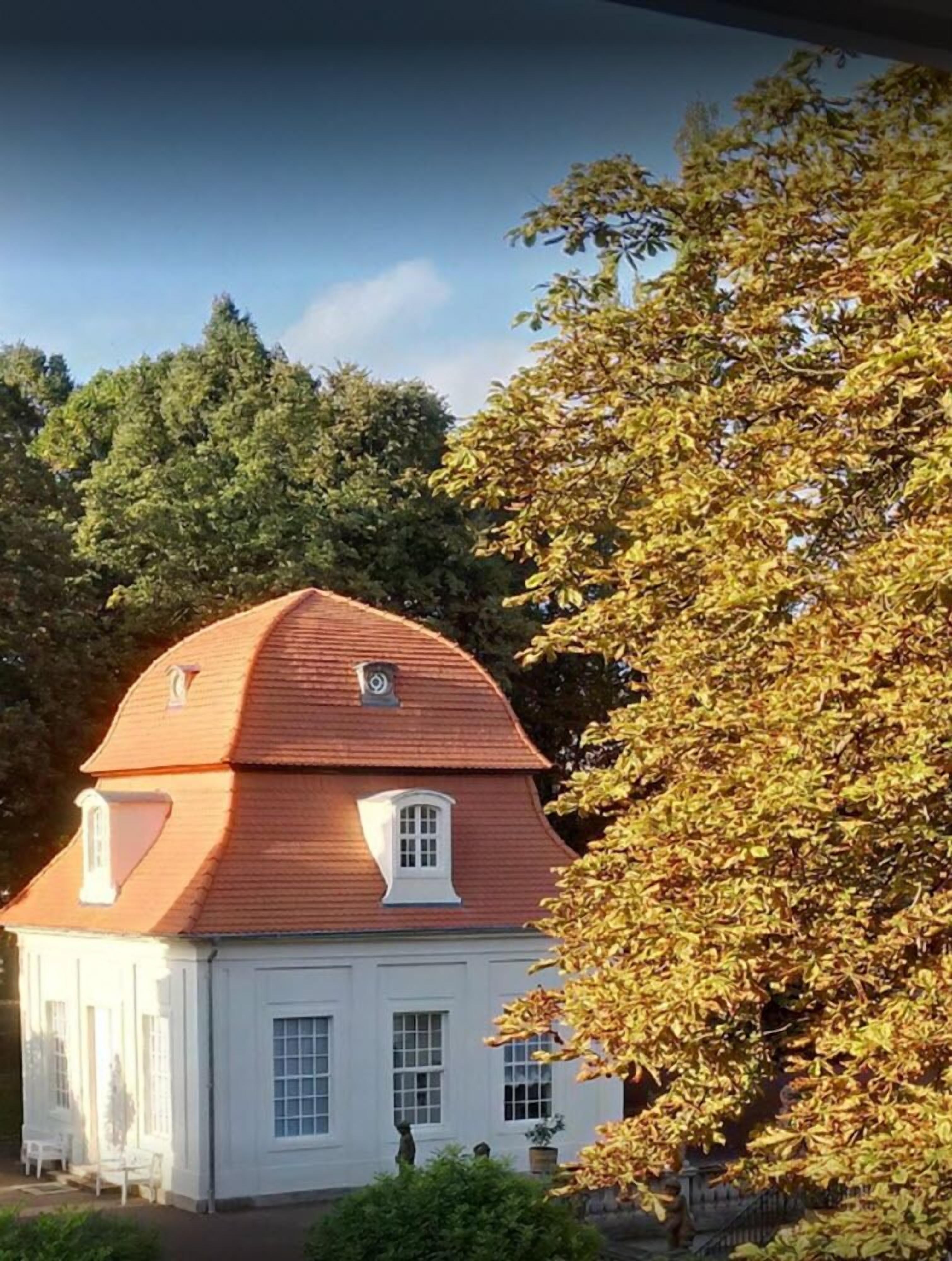 A white building with a red roof, surrounded by trees and greenery.