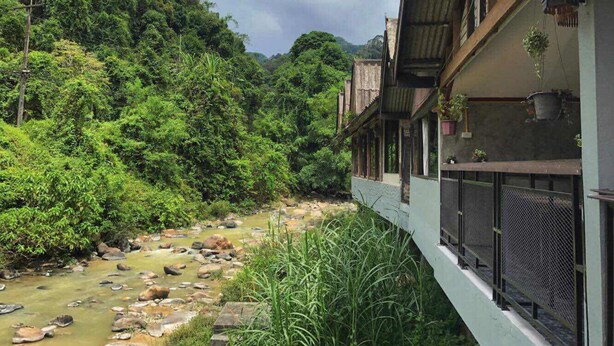 A riverside view with a building featuring balconies and hanging plants. - Thansila Resort (Ranong)