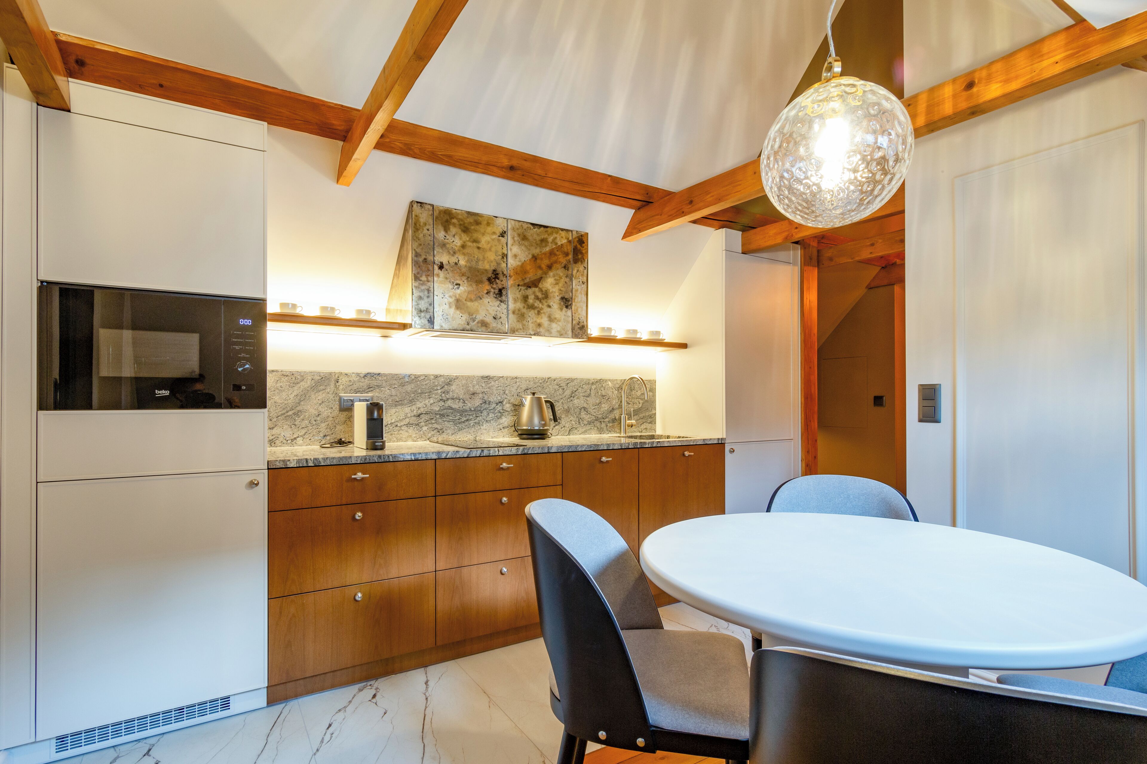 A modern kitchen with wooden cabinets, a marble countertop, and a dining area with a round table and chairs.