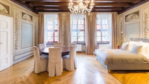 A room with a wooden floor, a dining table with chairs, a bed with pillows, and a chandelier.