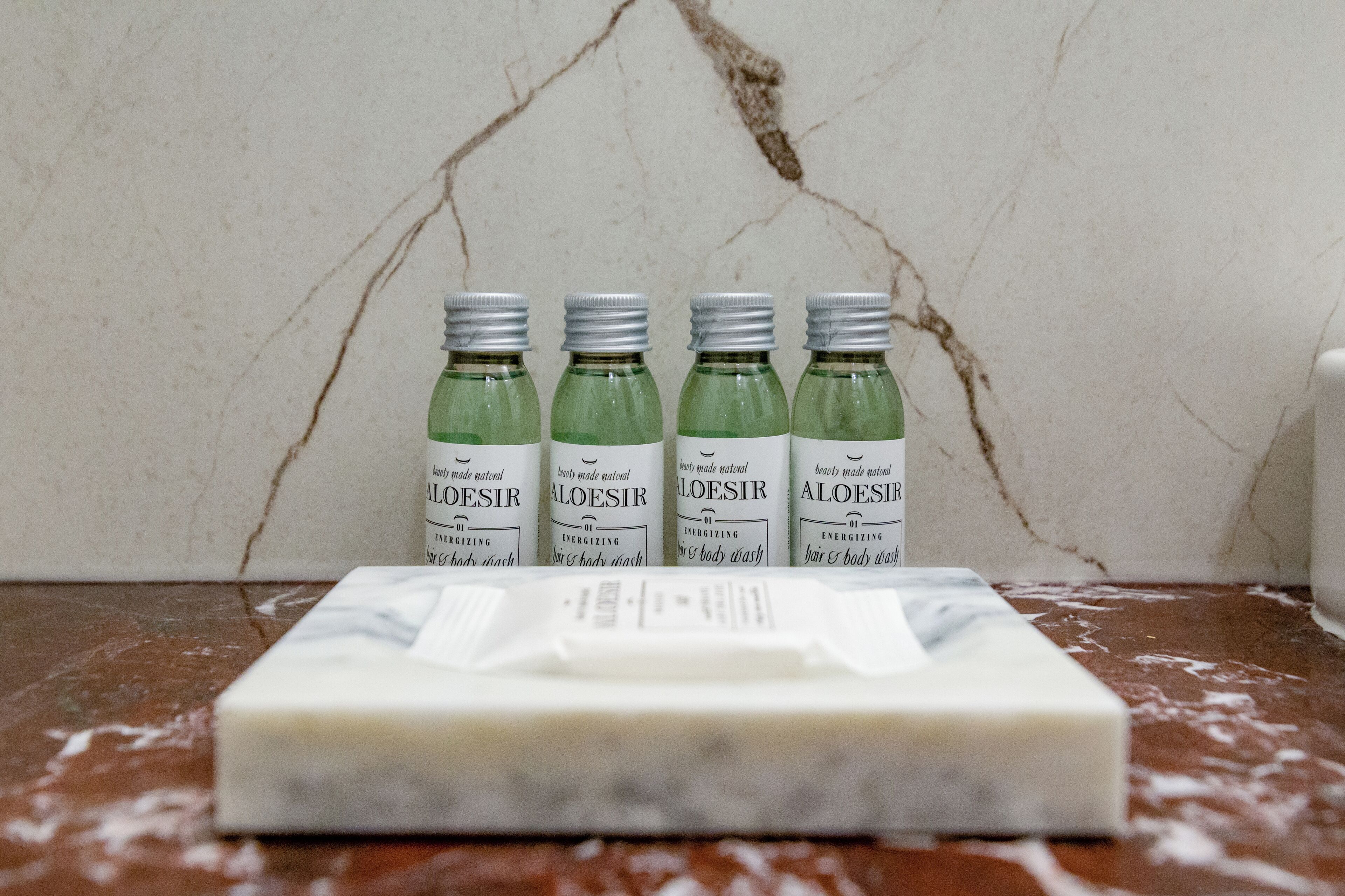 Four bottles of Aloesir body wash and a bar of soap on a marble surface.