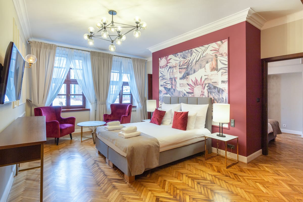 A hotel room with a large bed, a desk, two chairs, a chandelier, and a large floral wall mural.