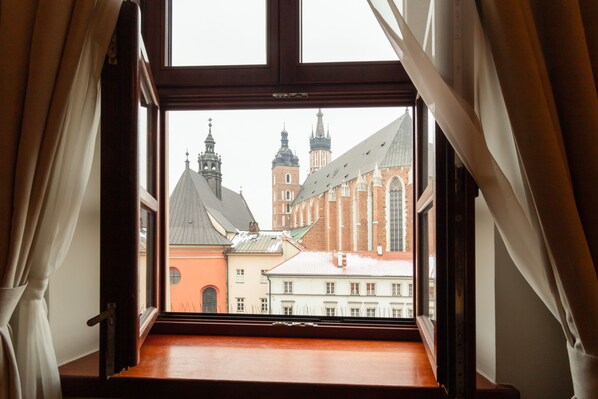 A view from a window with curtains, overlooking a building with multiple towers and a red facade.