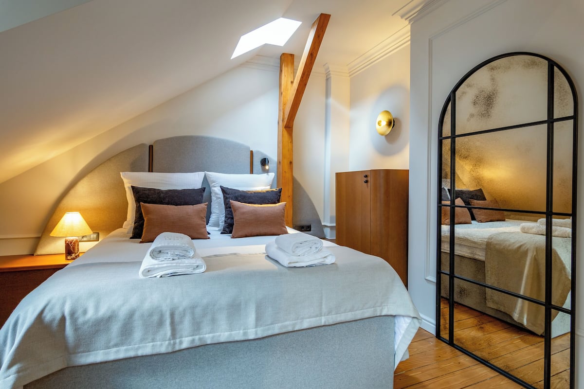 A bedroom with a skylight, a bed with neatly folded towels, a wooden wardrobe, and a mirrored wall.