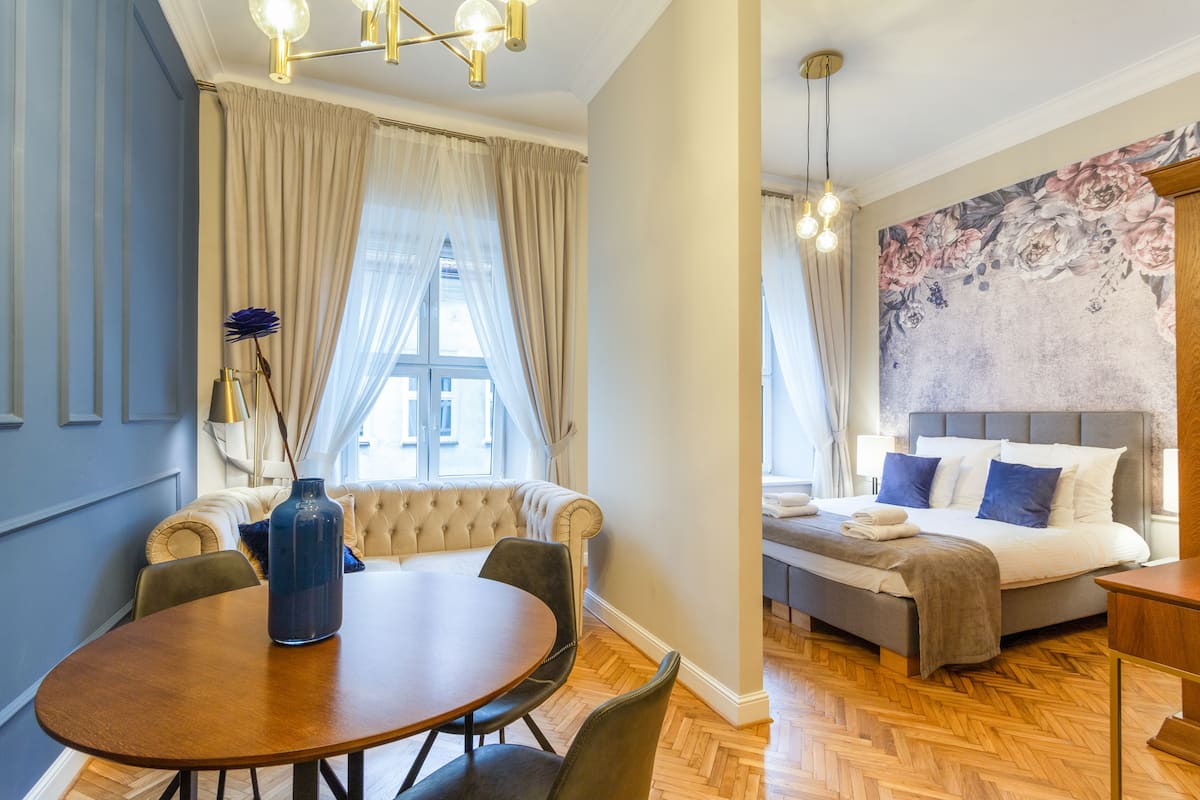 A hotel room with a dining area, a bed with a headboard, and a floral wall mural.