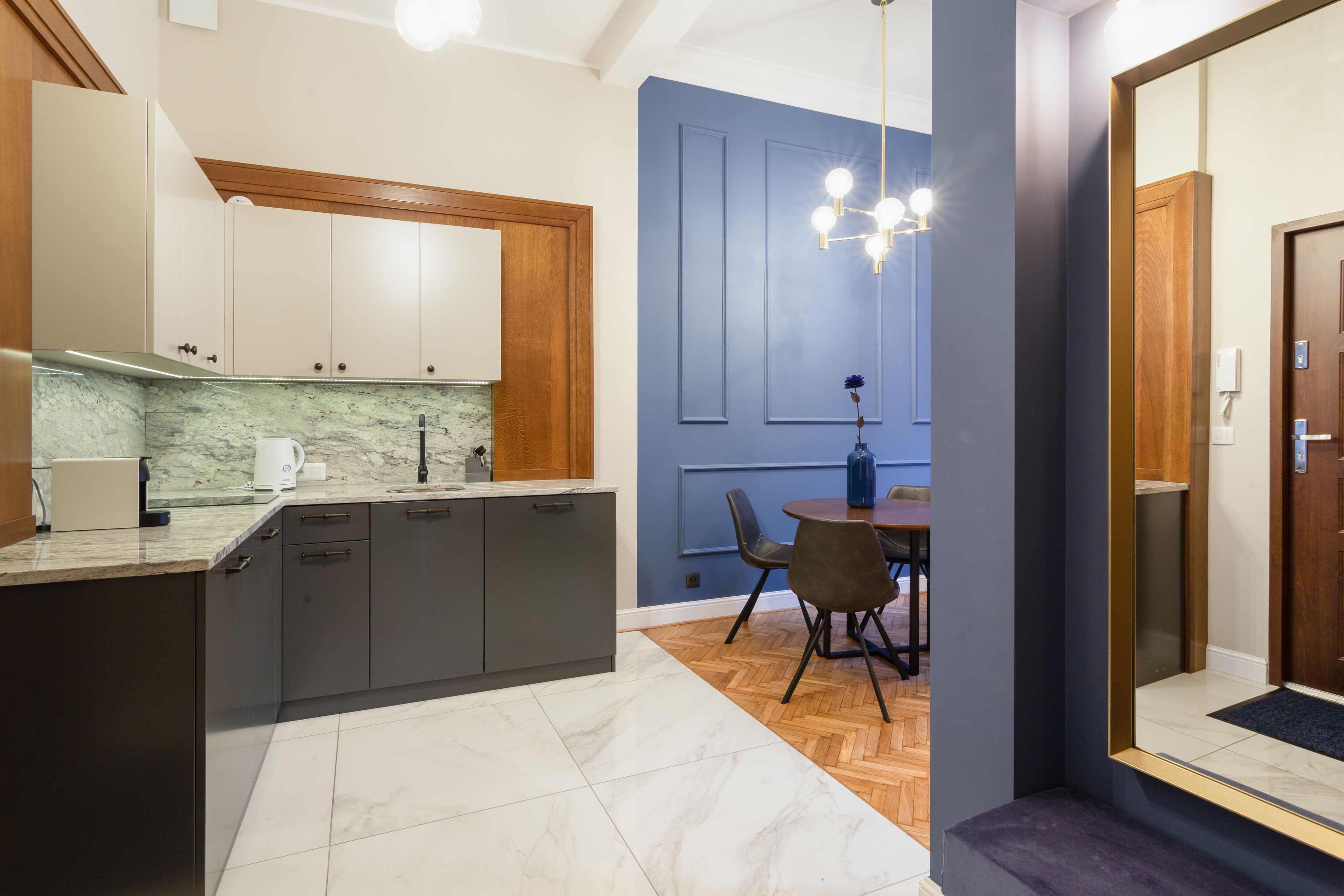A modern kitchen with grey cabinets, a marble countertop, and a dining area with a round table and chairs.