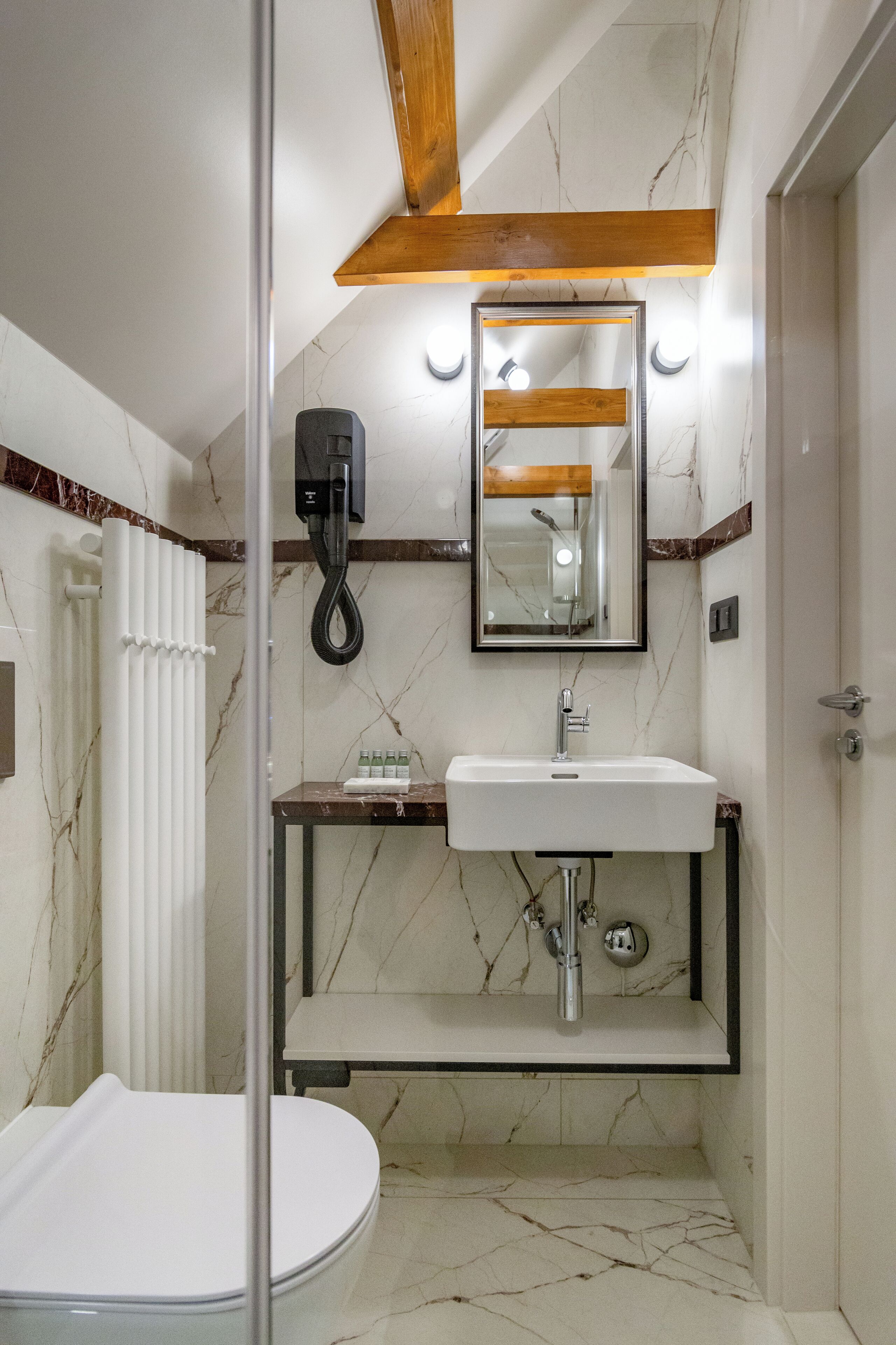 Ein modernes Badezimmer mit Marmorboden, Toilette in Weiß, Waschbecken mit Spiegel darüber und Duschbereich.