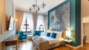 A hotel room with a bed, a desk, a chair, a table, and a painting on the wall.