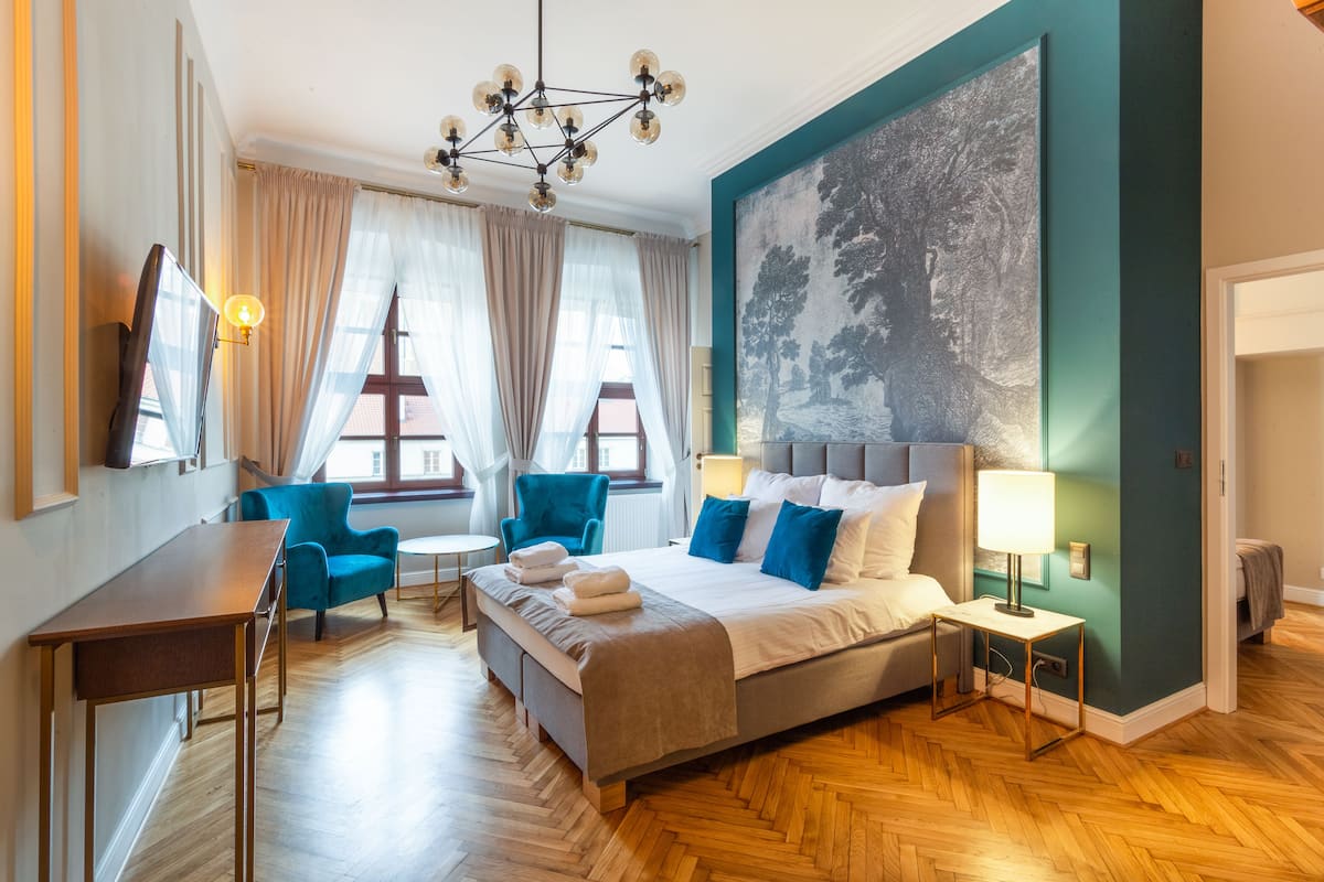 A hotel room with a bed, a desk, a chair, a table, and a painting on the wall.