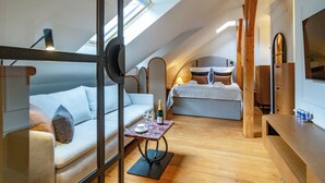 A cozy attic bedroom with a sloped ceiling, a bed, a sofa, and a small table with a bottle and glasses.
