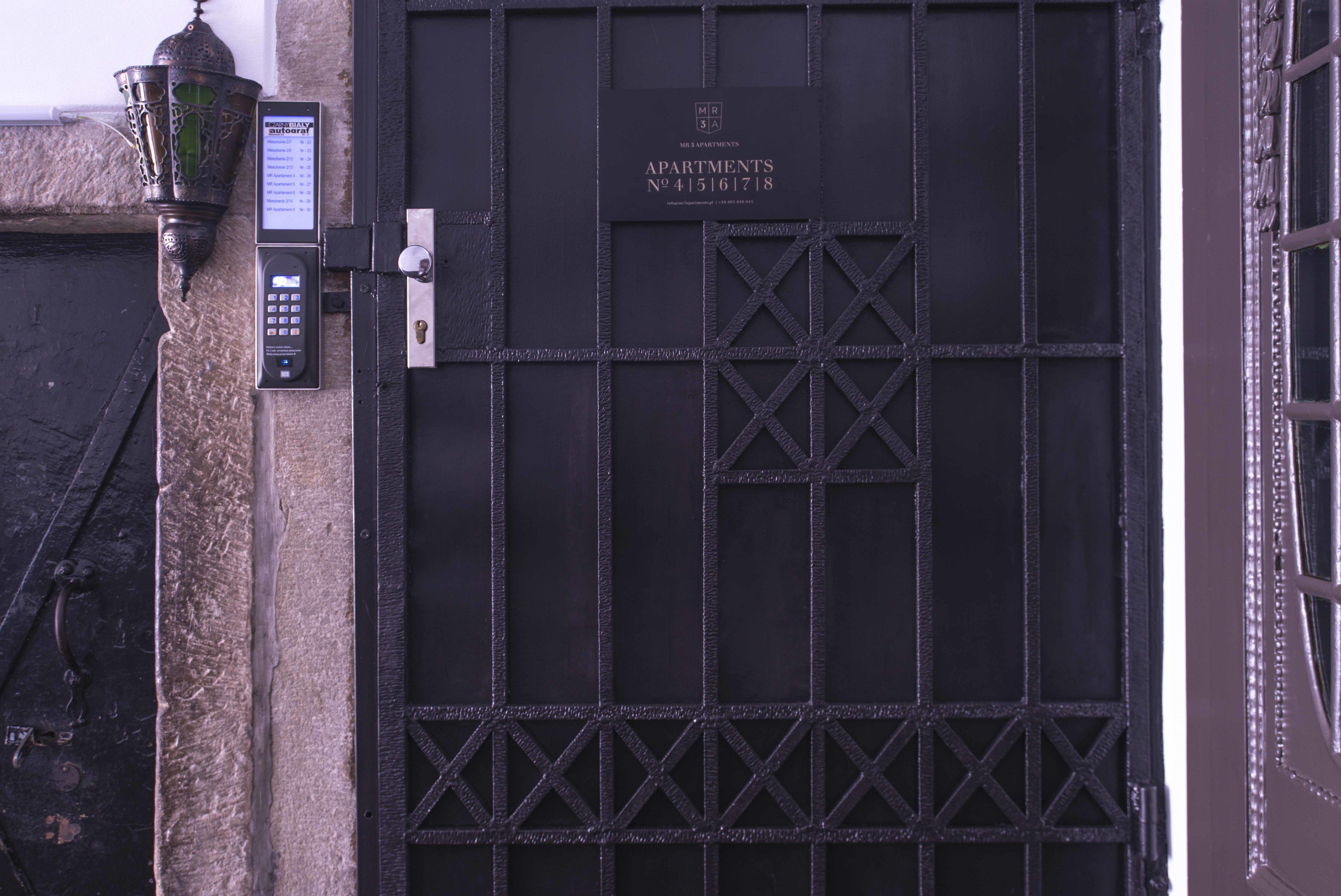 A black metal gate with a keypad and a sign above it.