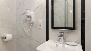 Un baño con pared de mármol, lavamanos blanco, cabina de ducha de vidrio y secador de pelo incorporado.