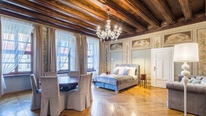 A room with a wooden floor, a bed, a sofa, a table with chairs, and a chandelier.