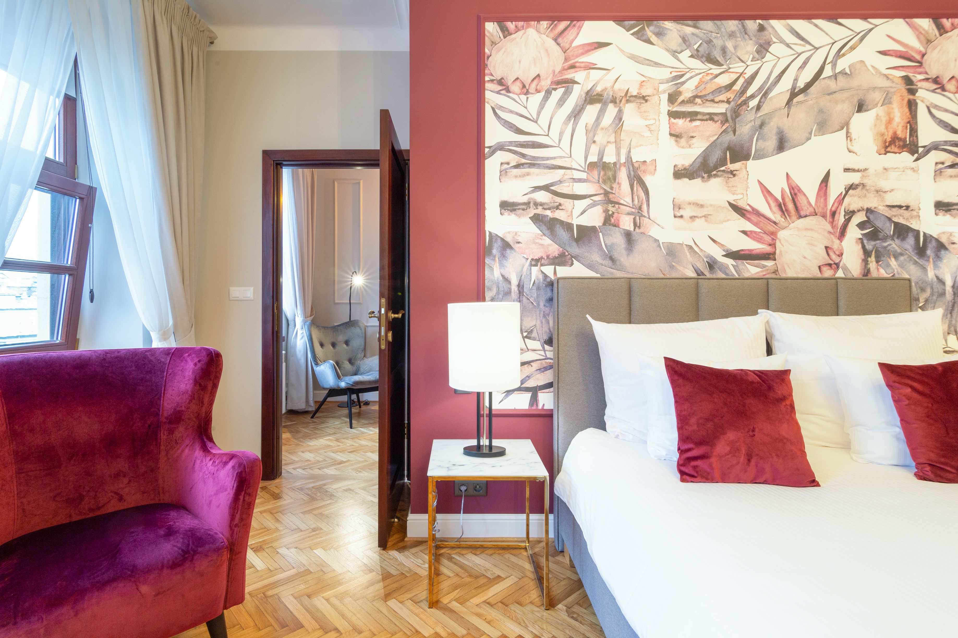 A hotel room with a bed, a chair, a nightstand, and a wall with a tropical leaf pattern.