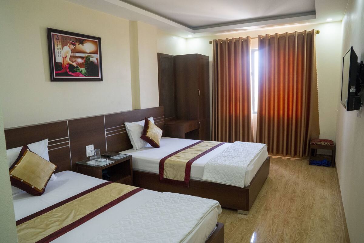 A hotel room with three beds, a wardrobe, a television, and a painting on the wall.