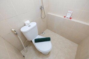 A small, clean bathroom with a toilet, a shower, and a shelf with toiletries. - Monochrome Style 2 Bedrooms at Kalibata City Apartment By Travelio (Jakarta)
