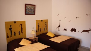 Une chambre avec deux lits, chacun agrémenté d’un oreiller jaune et d’une couverture marron. Un mur est décoré de silhouettes d’animaux, et un tableau est accroché au-dessus des lits.