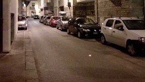 Una calle estrecha flanqueada por vehículos estacionados y edificios.