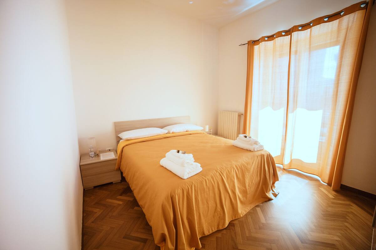 Ein Hotelzimmer mit einem Bett, einem Nachttisch, einer Lampe und einem Fenster mit Vorhängen.