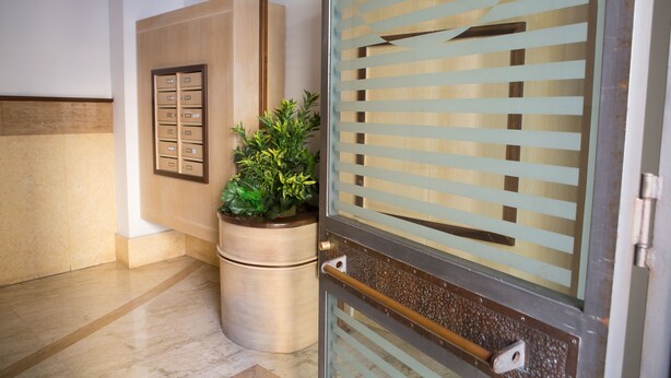 Un vestíbulo moderno con puerta de cristal, un mueble de madera con cajones y una planta en maceta.