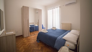 Una habitación de hotel con cama, escritorio, espejo y aire acondicionado.