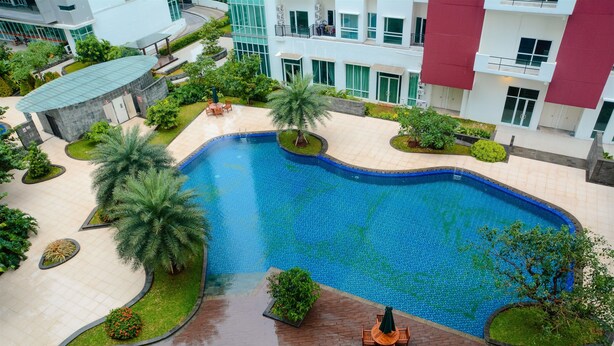 A swimming pool surrounded by palm trees and greenery, with a building in the background. - 2 Bedrooms Woodland Park Apartment by Travelio (Jakarta)